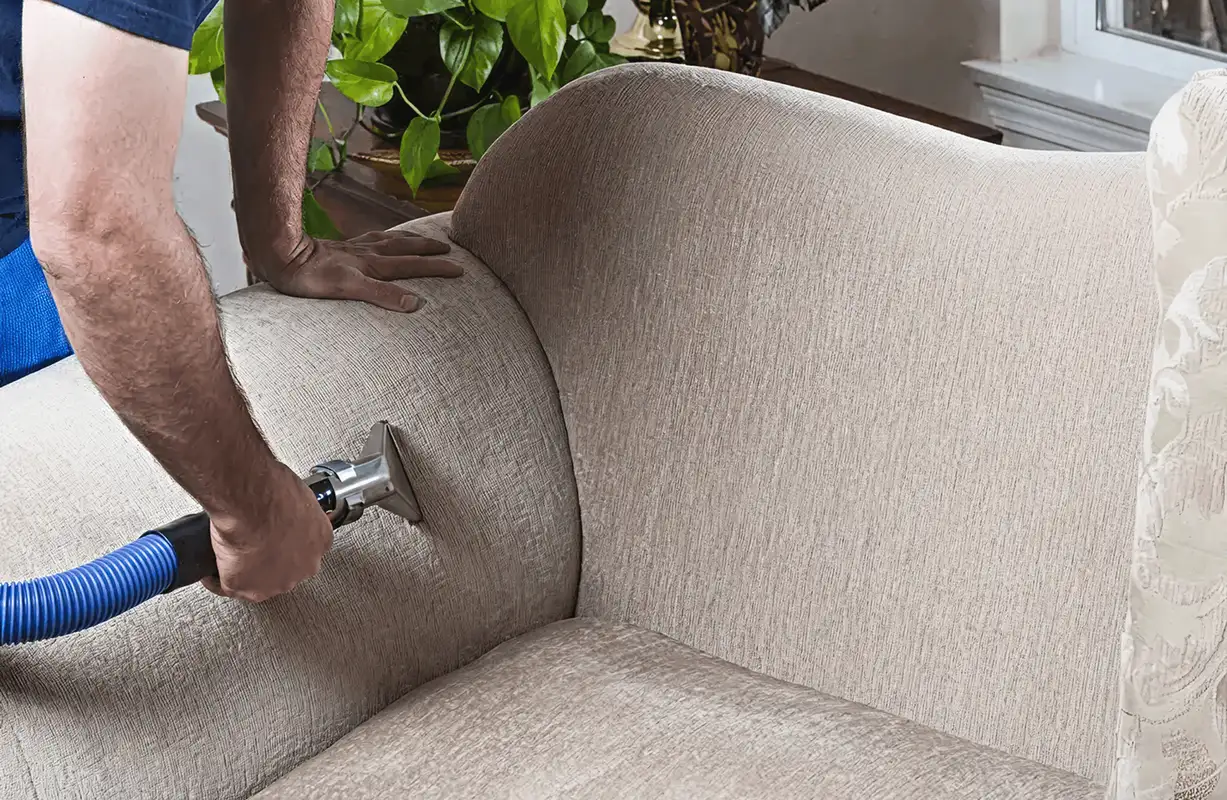 Professional upholstery cleaner deep-cleaning a fabric sofa with a handheld extraction tool and hose, Dallas, TX.